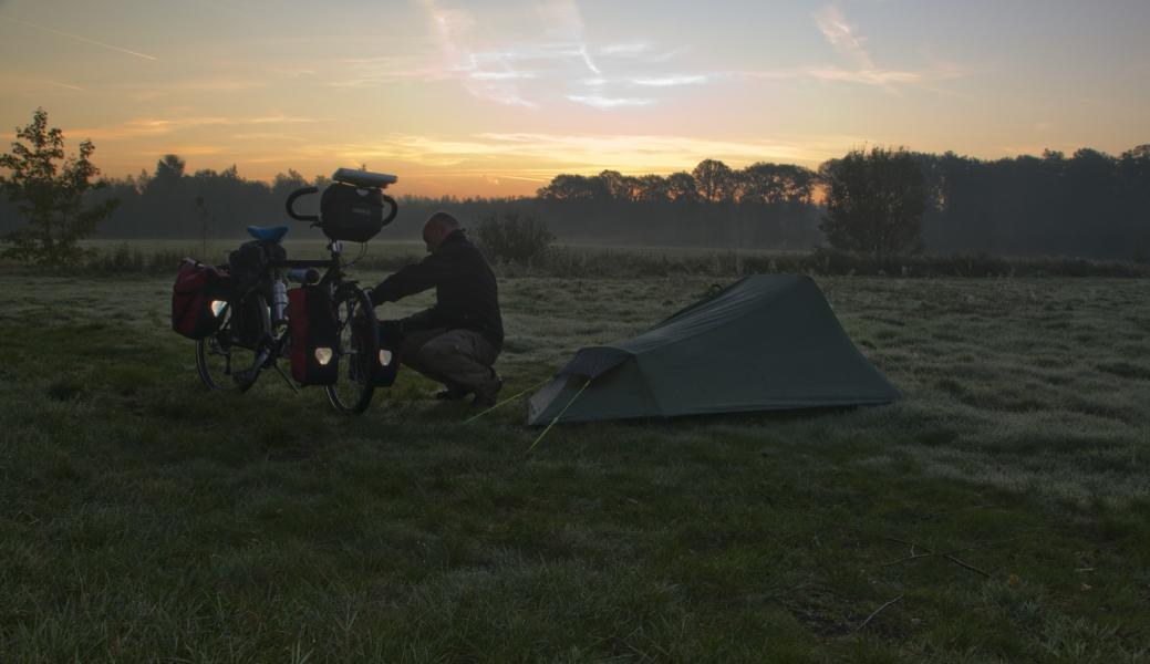 fietser bij zijn tent bij zonsondergang