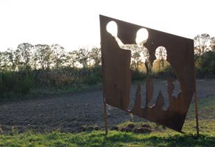 Ijzeren bord met gat in de vorm van twee spelende kinderen, de kinderen worden ingekleurd door het natuurlandschap erachter